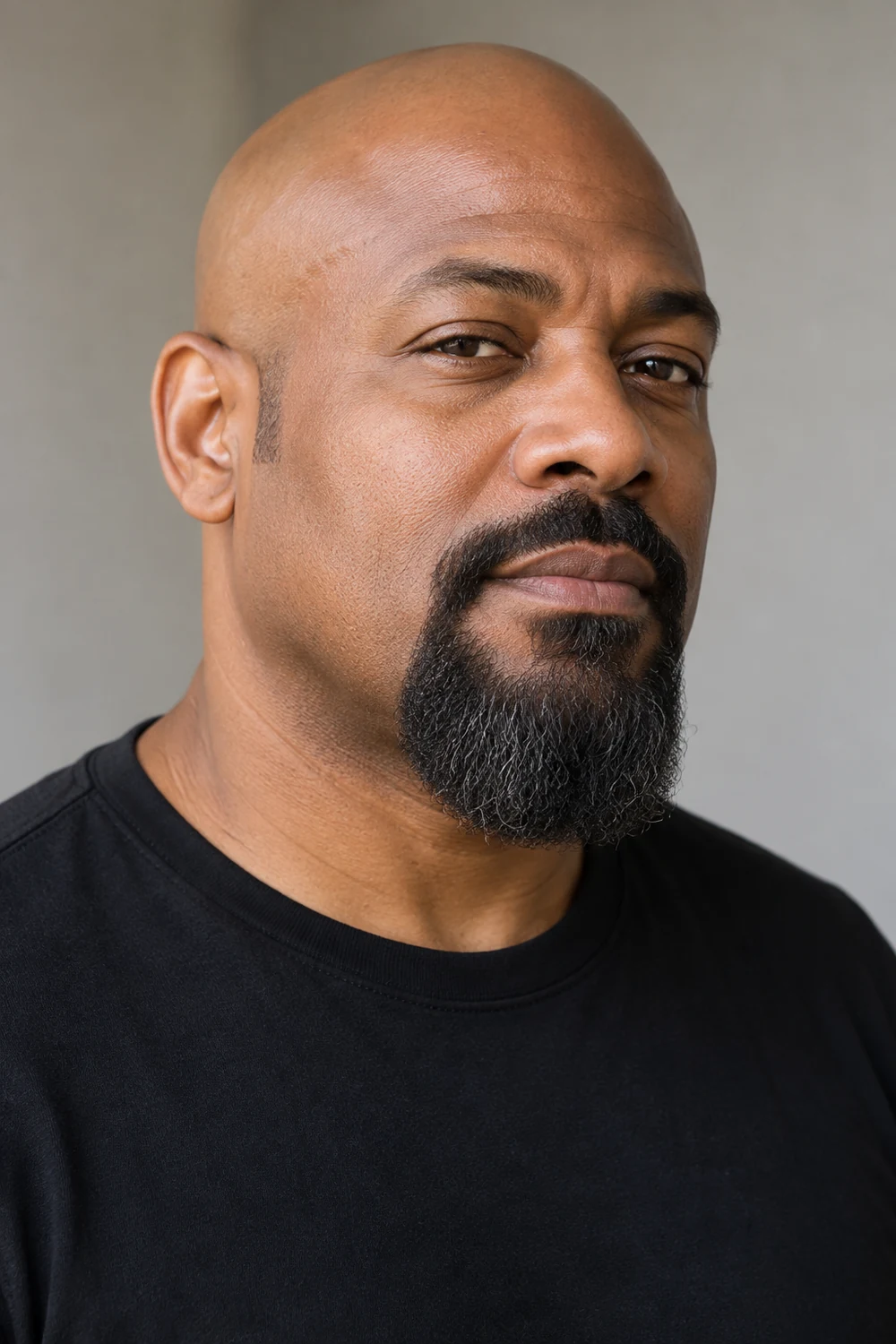 Fictional bald adult man with medium-dark skin, a broad rounded goatee, bare cheeks, short separate sideburns, and a connected short mustache.