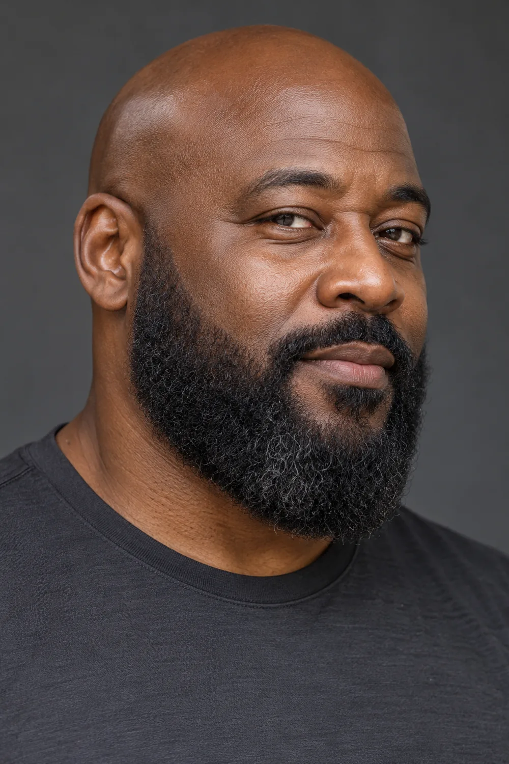 Fictional adult Black man with a bald head and a dense, rounded full beard, photographed in three-quarter view.