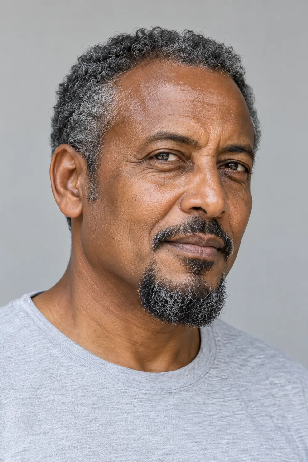 Mature man with salt-and-pepper curls wearing a compact disconnected goatee, narrow separated mustache, and clean-shaven cheeks.