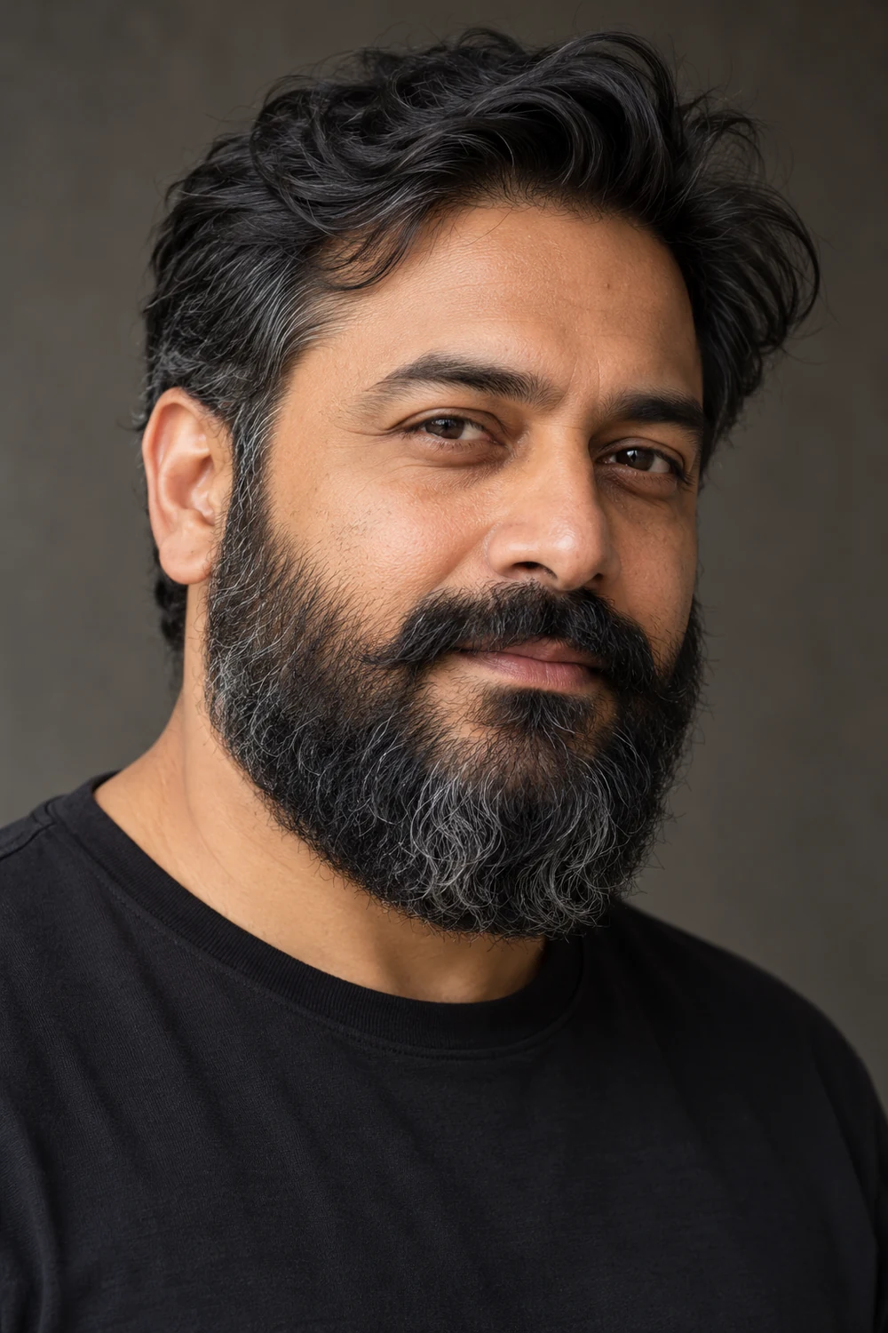 Three-quarter portrait of an adult South Asian man with a dense, wavy rounded full beard and connected mustache.