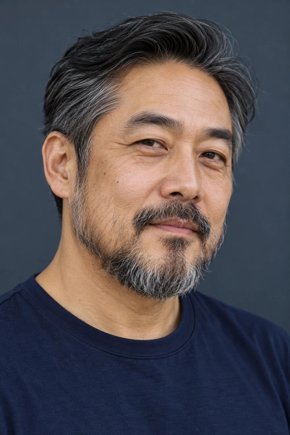 Three-quarter portrait of a middle-aged East Asian man with a rounded salt-and-pepper beard, sparse cheek growth, a softly defined upper cheek line, and a mustache with faint corner connections.