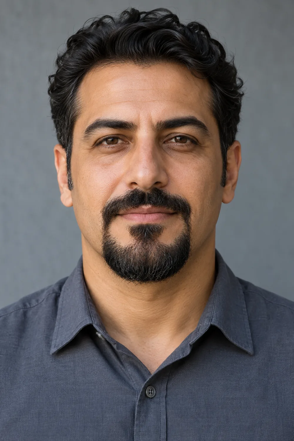 A man with a compact rounded connected goatee and mustache, clean-shaven cheeks, and short separate sideburns.