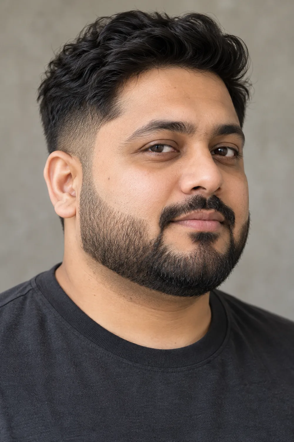 Fictional adult South Asian man with a round face, short squared boxed beard, trimmed cheek lines, and connected mustache, wearing a charcoal crew-neck shirt.
