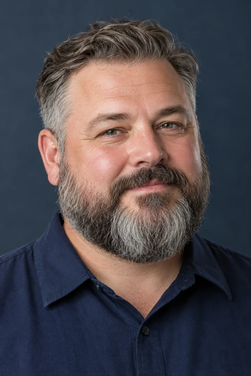 Fictional adult man with a round face wearing a broad, rounded salt-and-pepper full beard and joined mustache.