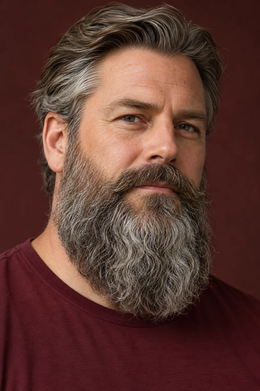 Three-quarter portrait of an adult man in a burgundy shirt with a long, wavy salt-and-pepper beard, rounded bottom, and full connected mustache.