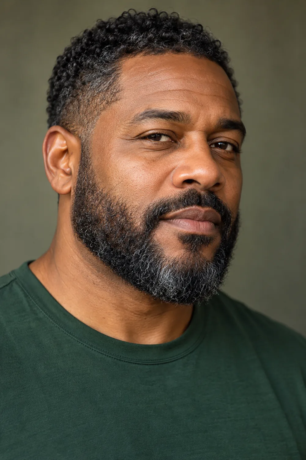 Three-quarter portrait of an adult Black man with a compact salt-and-pepper beard, low natural cheek line, softly rounded chin, and close connected mustache.