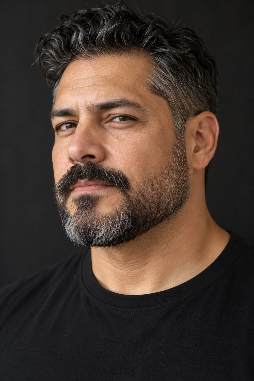 Three-quarter portrait of an adult man with a short dark-and-gray beard, rounded chin, and thick connected chevron mustache.