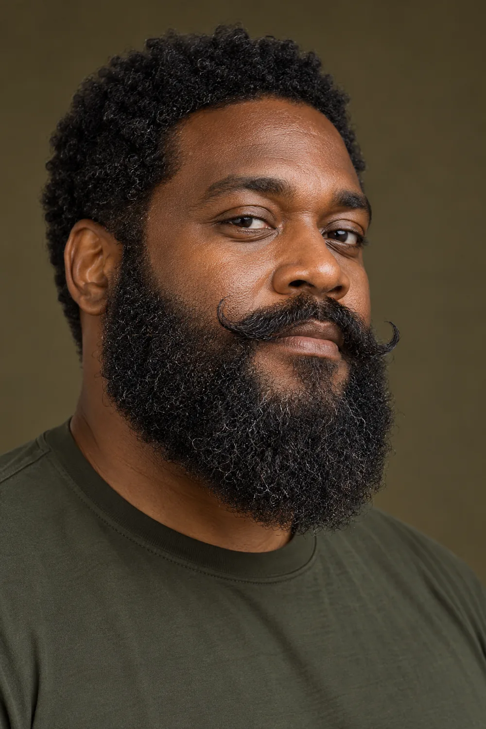 Three-quarter portrait of an adult Black man wearing a full, tightly curled rounded beard and a medium-width handlebar mustache with upturned tips, in a dark olive shirt.