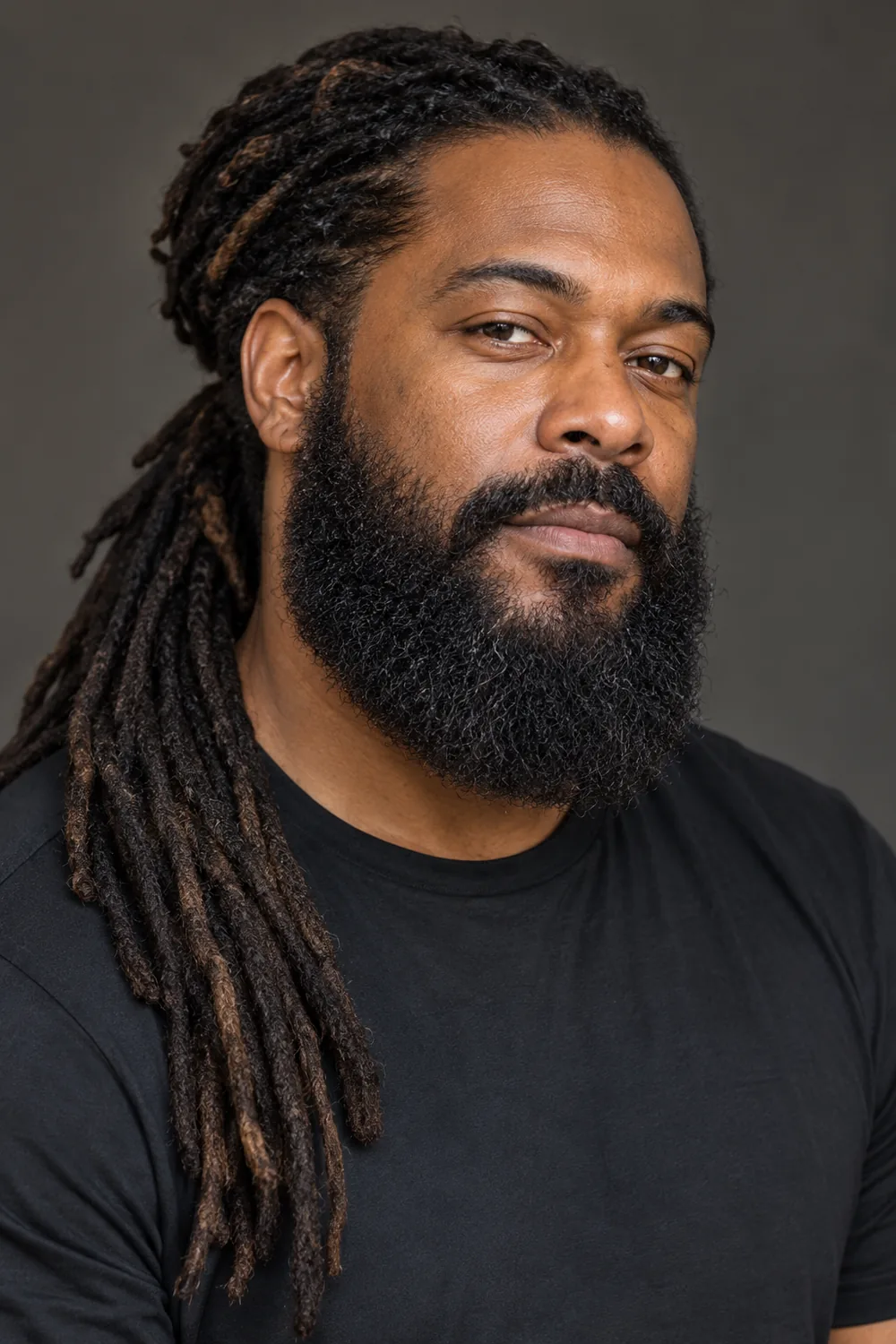 Fictional adult Black man with long tied-back locs over one shoulder and a dense rounded full beard with a connected mustache.