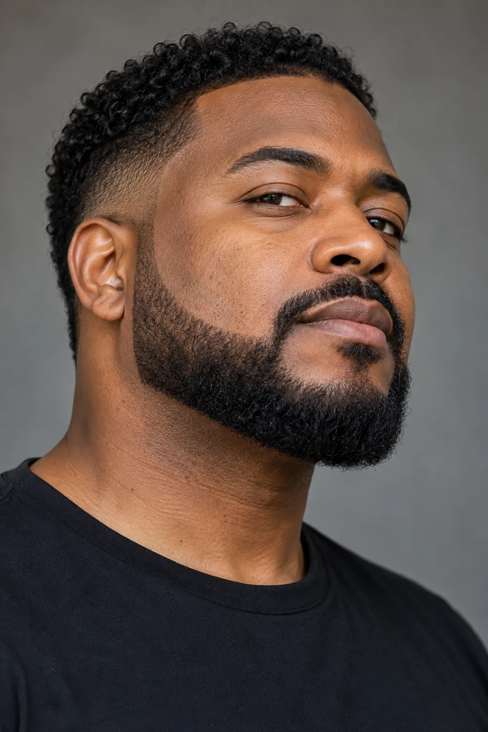 Three-quarter portrait of an adult Black man with a broad chin strap beard, crisp high cheek line, faded sideburns, connected mustache, and rounded chin contour.