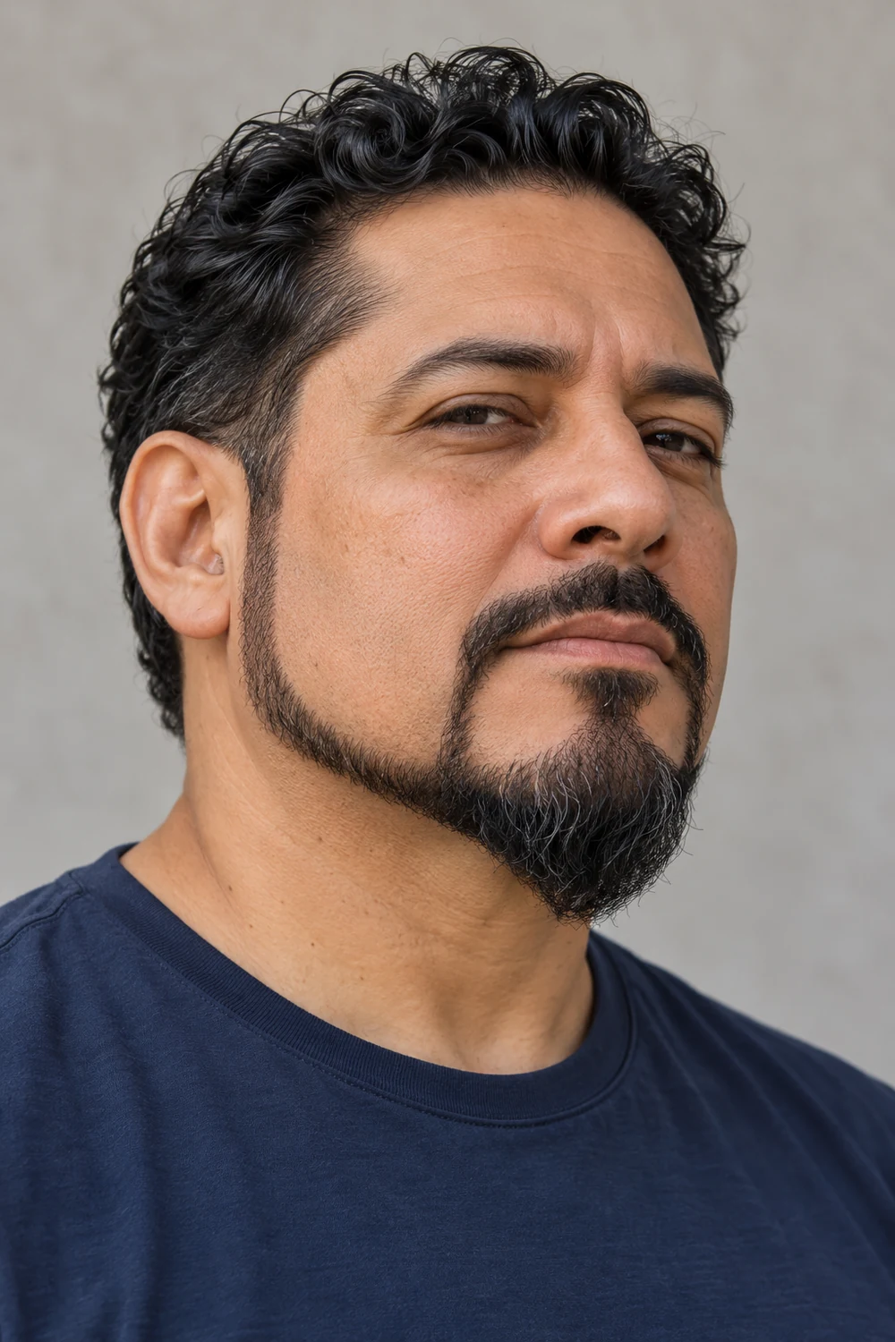 Adult man in a three-quarter portrait with a narrow chin strap beard, connected short mustache, and fuller rounded chin section.