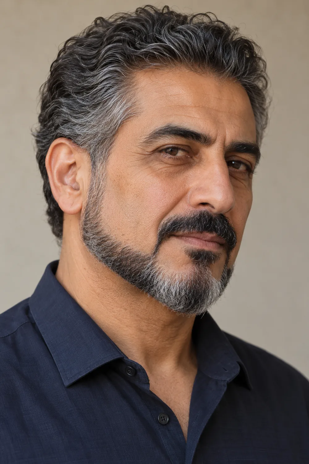Mature man with warm tan skin, a wide salt-and-pepper chin strap beard tapering to a soft point, and a separate mustache.