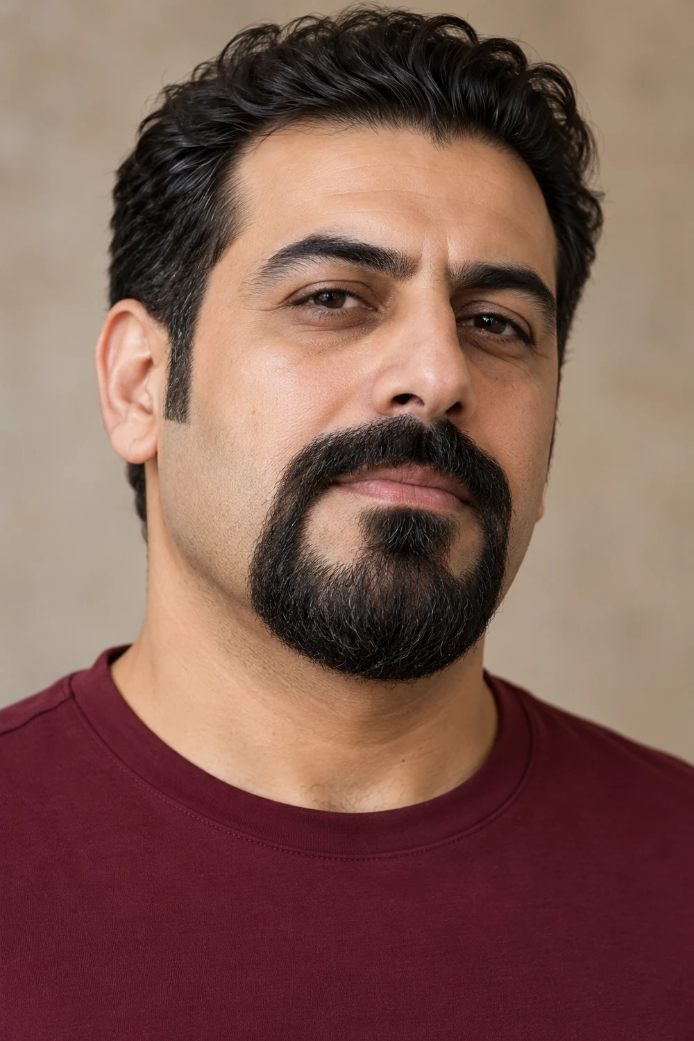 Adult man with a broad dark mustache connected at both mouth corners to a rounded circle beard, clean cheeks and a burgundy shirt.