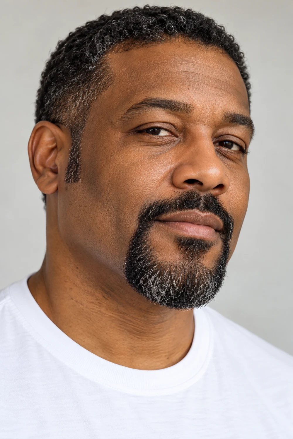Three-quarter portrait of an adult Black man with a compact rounded circle beard, connected mustache, high shaved cheek line, and slight gray at the chin.