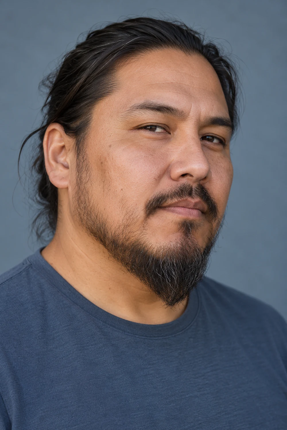 Three-quarter portrait of an adult man with sparse cheek growth and a short-medium ducktail beard tapering to a soft point beneath his chin.