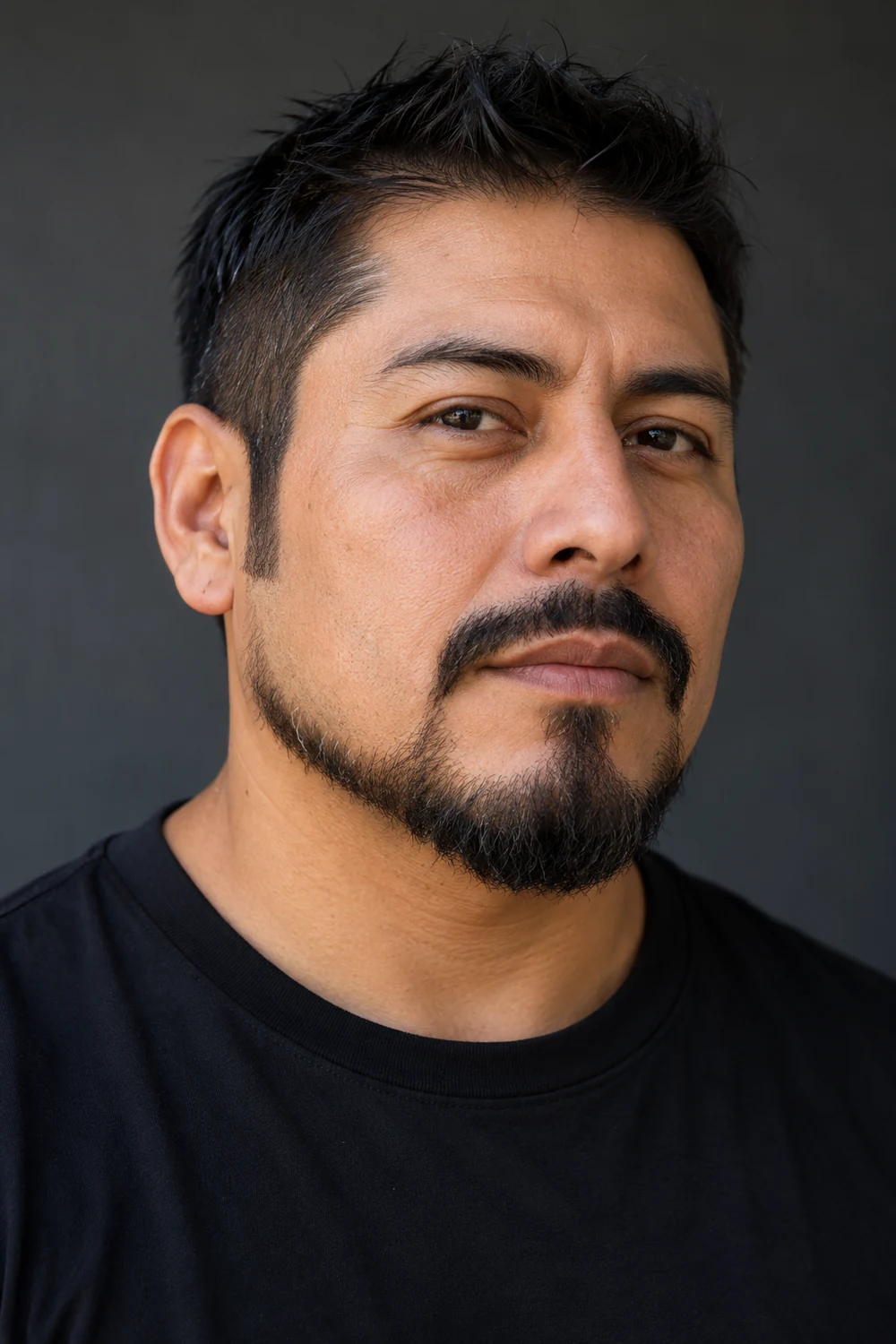 Three-quarter portrait of an adult man with a short extended goatee, shaved upper cheeks, tapered disconnected sideburns, and a compact chin beard; the mustache is nearly joined at the mouth corners.