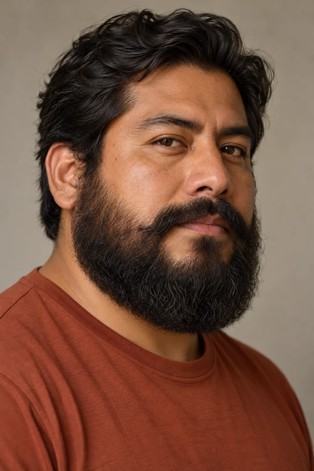 Three-quarter portrait of an adult man with a broad, rounded dark beard and a full connected mustache, wearing a rust-colored shirt.