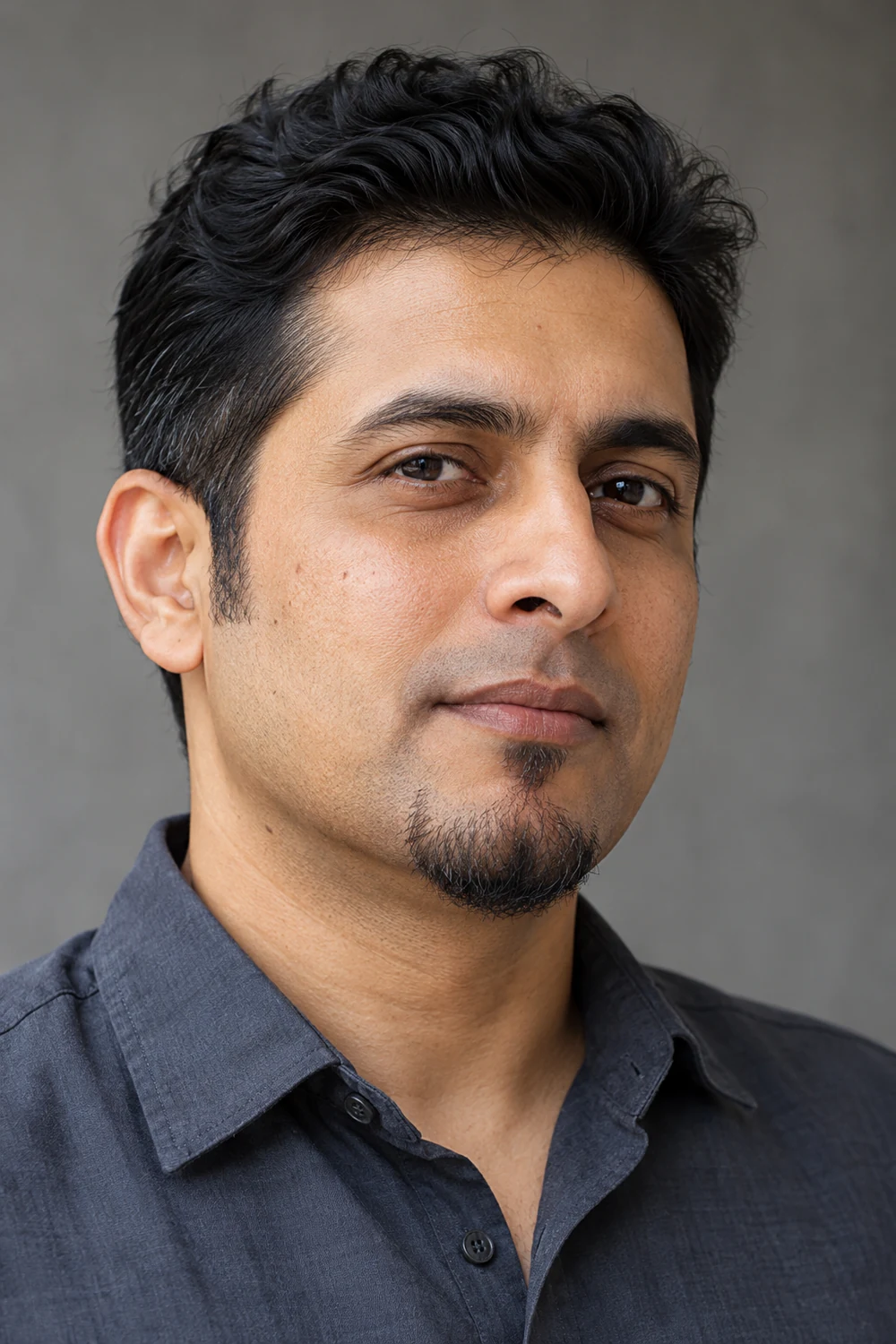 Three-quarter portrait of a South Asian man with naturally sparse short chin hair, a separate soul patch, and a clean-shaven upper lip.