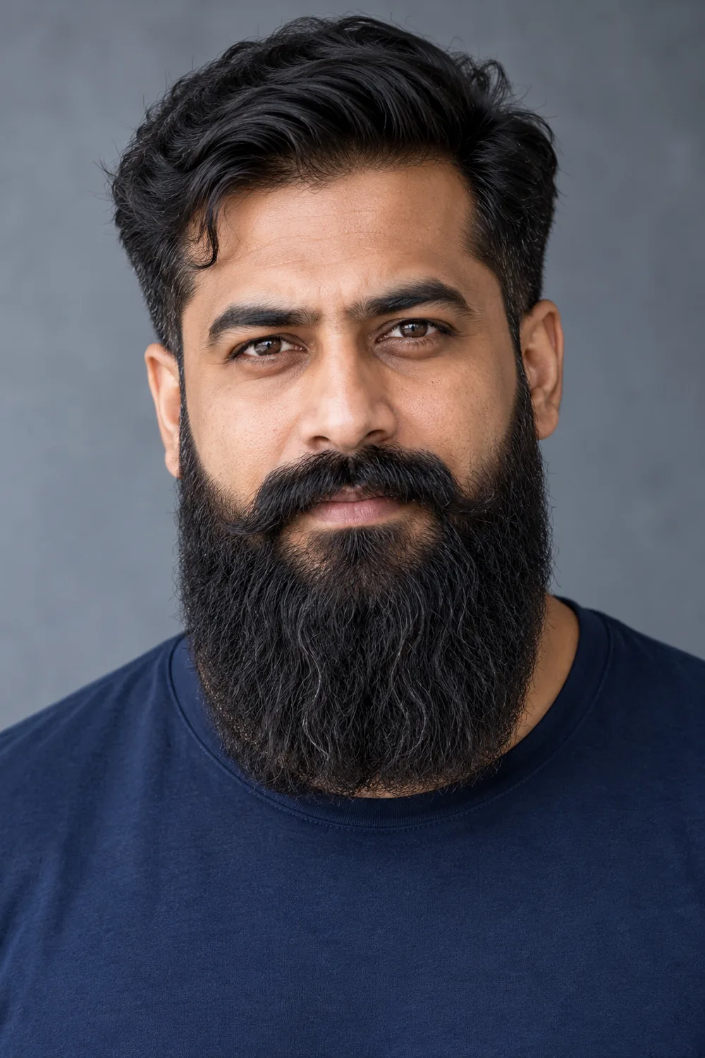 Fictional adult South Asian man in a frontal portrait wearing a navy shirt, with a long, broad squared beard, defined cheek lines, and a connected mustache with curled ends.