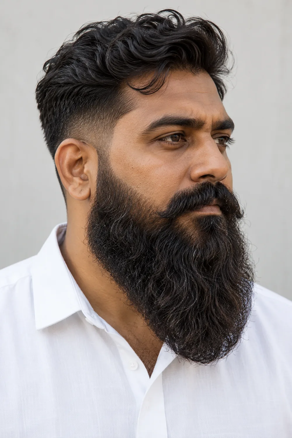 Side three-quarter portrait of an adult South Asian man with a full, wavy long beard, tapered upper sides, a rounded tip, and a connected mustache.