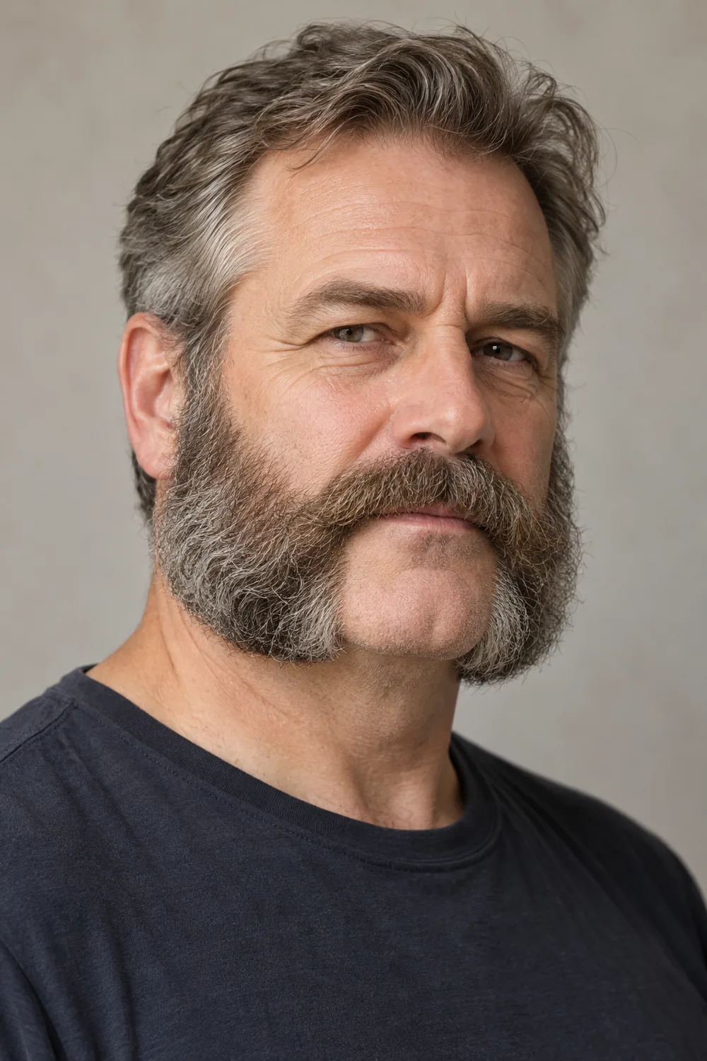 A gray-haired adult man in a dark crew-neck shirt, shown in three-quarter view with broad mutton chops connected to a full mustache and a clean-shaven chin.