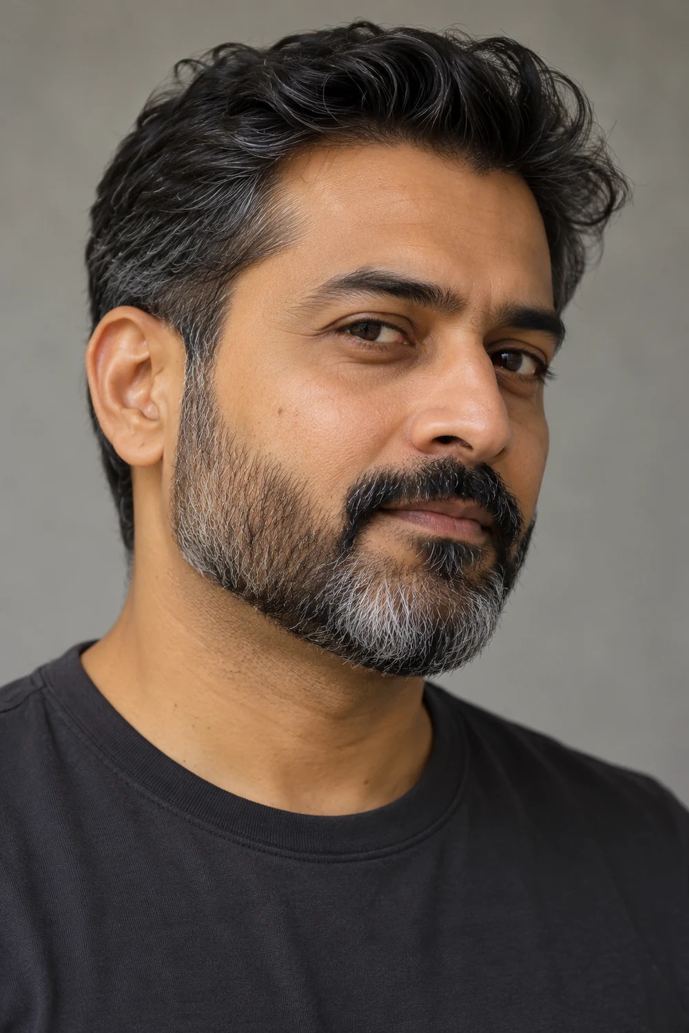 Three-quarter portrait of an adult man with a compact dark brown and gray boxed beard, connected mustache, crisp cheek line and charcoal crew-neck shirt.