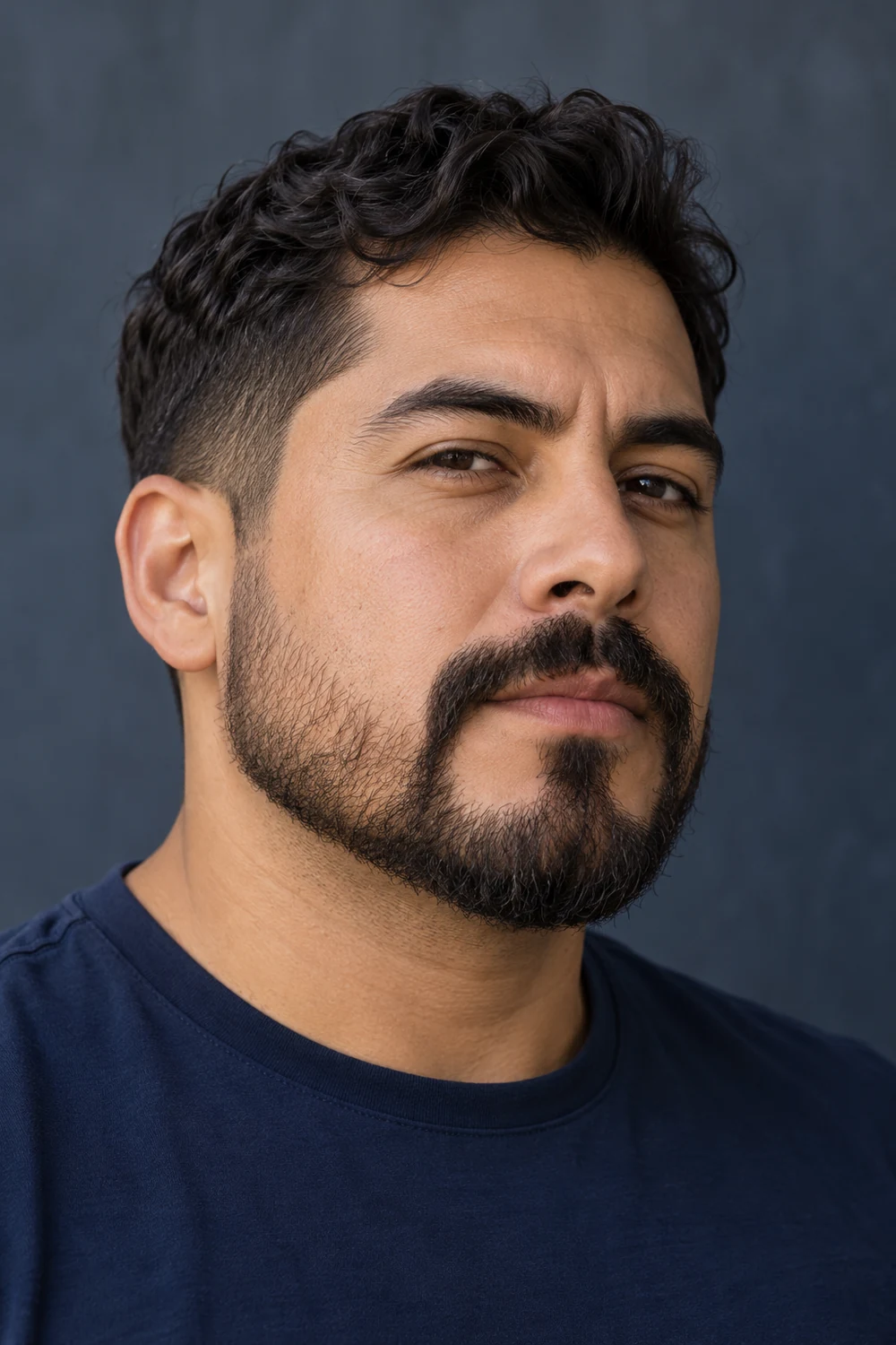 Three-quarter portrait of an adult man in a dark blue shirt, wearing a short beard with a broad chin and connected horseshoe mustache.