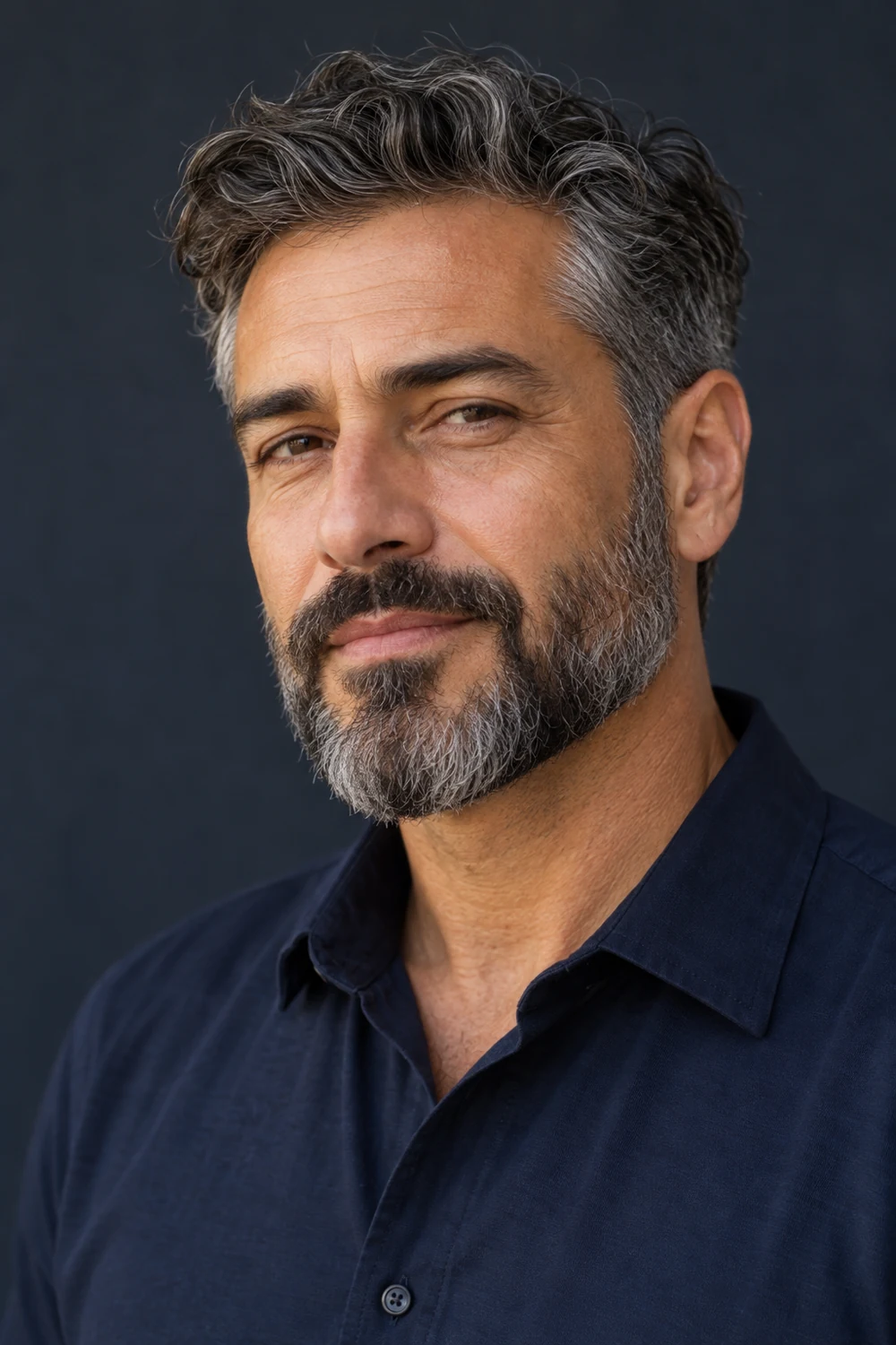 Three-quarter portrait of an adult man with a compact salt-and-pepper short boxed beard, softly tapered chin, clean cheek line, and connected mustache.