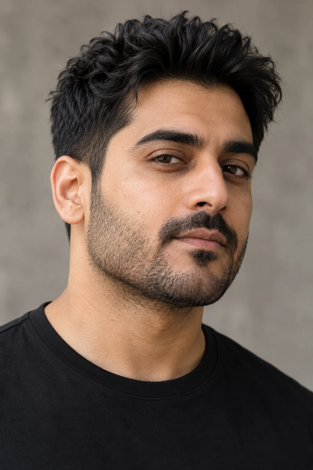 Fictional adult South Asian man in a black shirt, shown in three-quarter view with dense short stubble, a connected mustache, and a broad jaw.