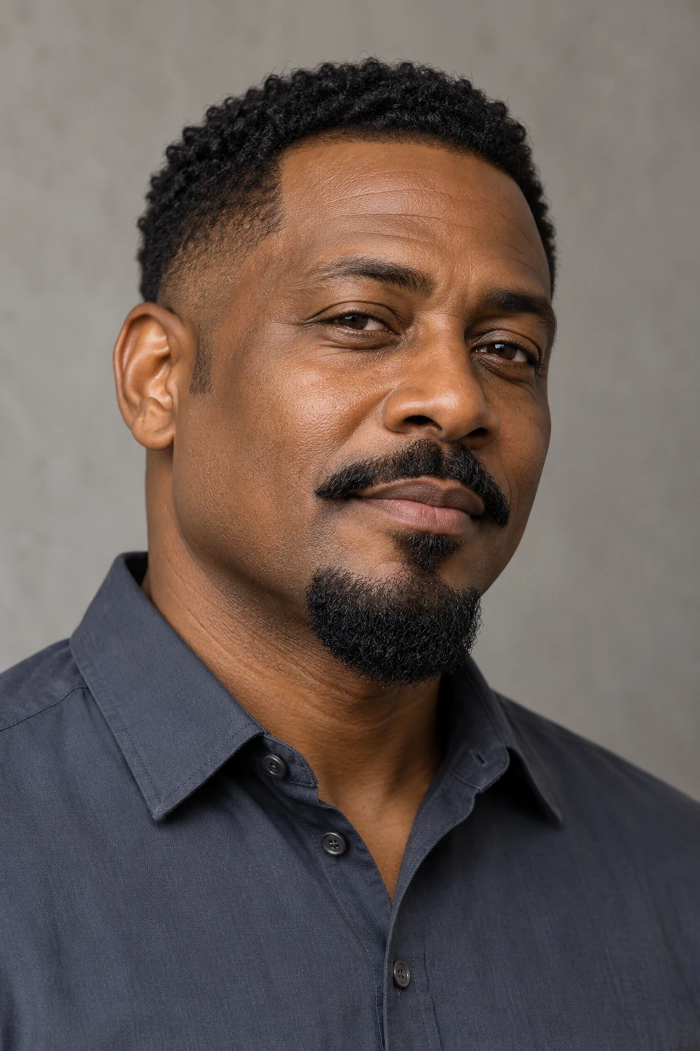 Three-quarter portrait of an adult Black man with a rounded chin beard, full disconnected mustache, clean-shaven cheeks, and short tapered sideburns.