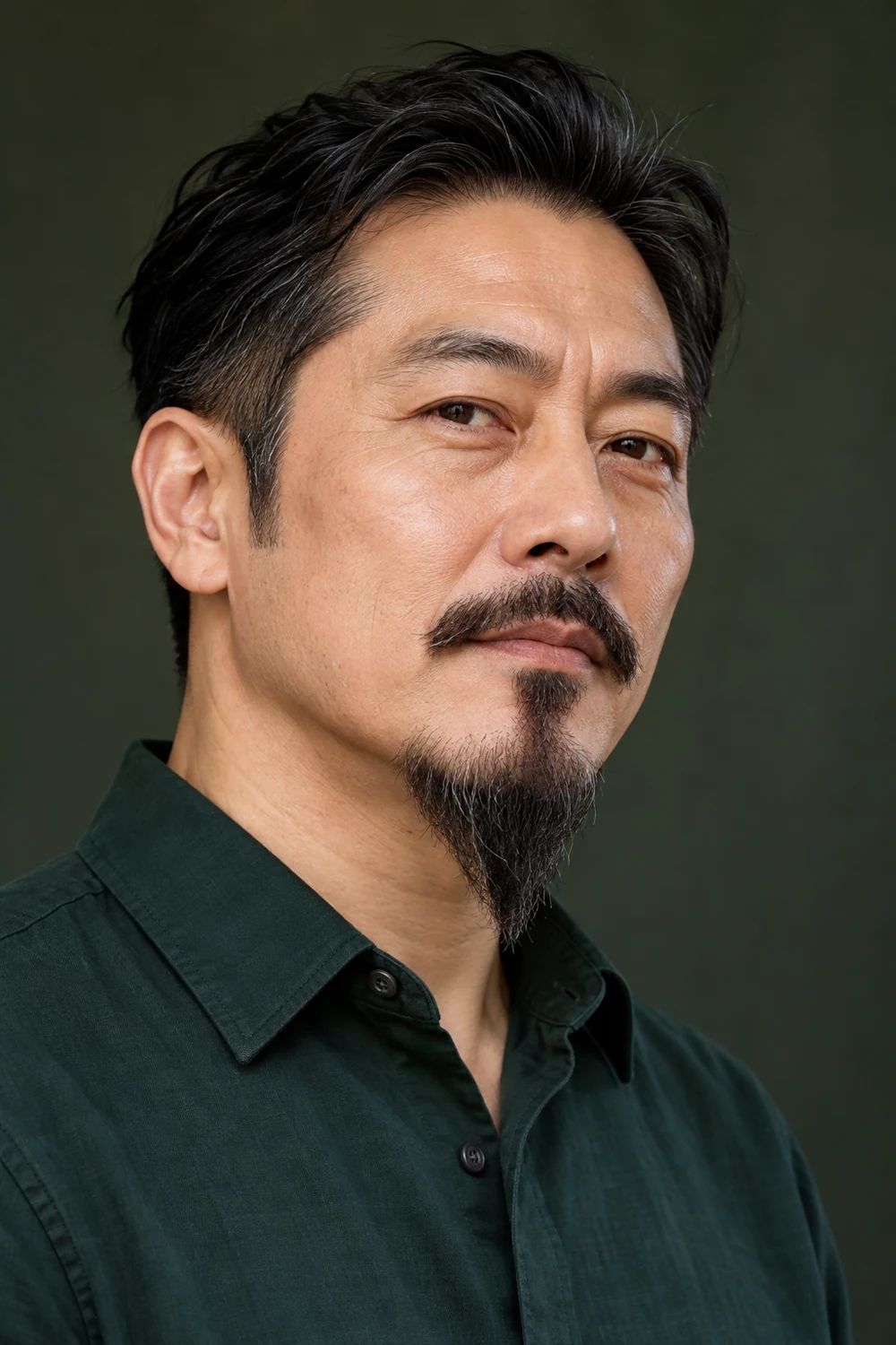 Adult East Asian man in a dark green shirt with clean-shaven cheeks, a separate mustache, and a long pointed chin beard.