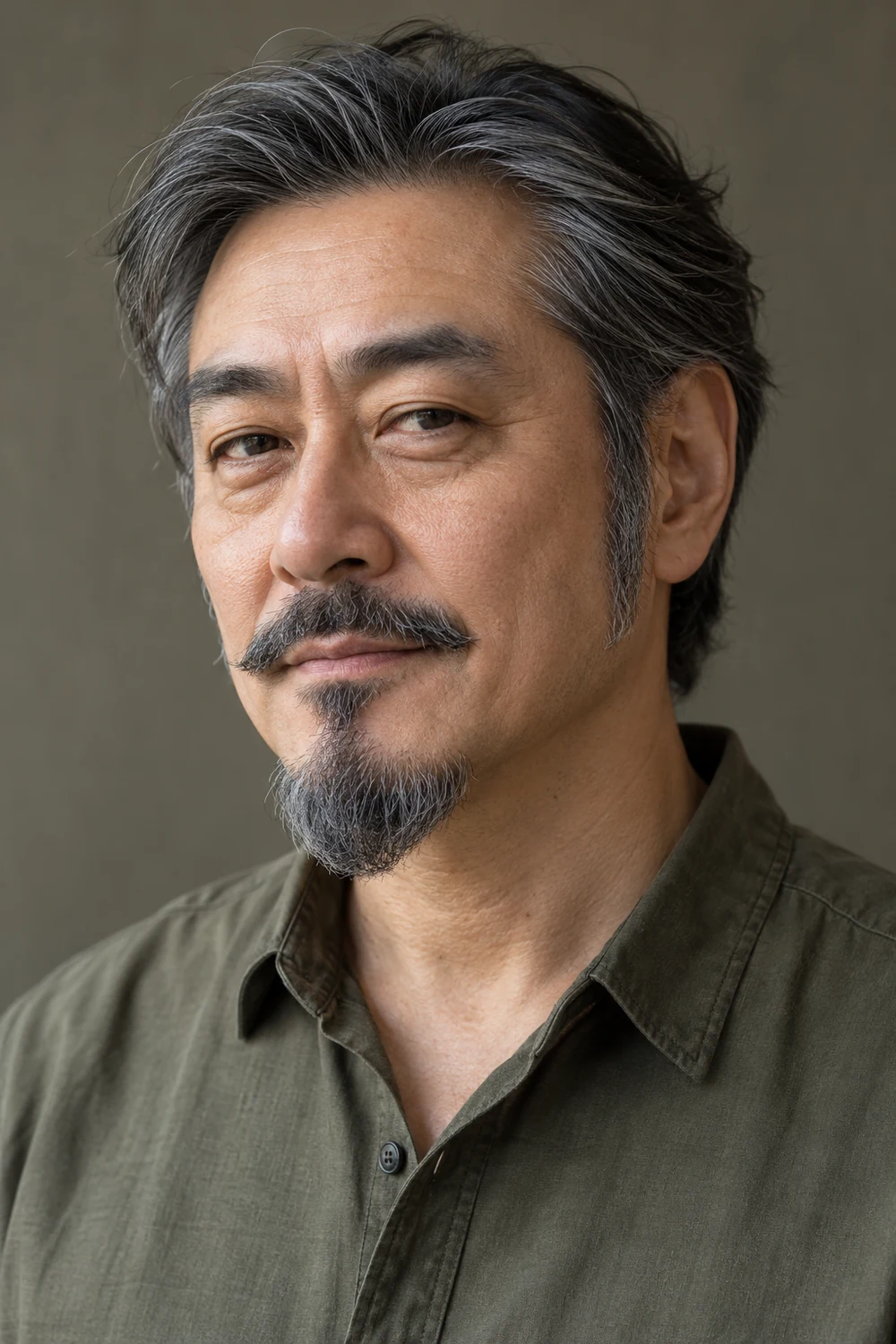 Three-quarter portrait of an adult Japanese man with long tapered sideburns, clean-shaven cheeks, and a separate rounded salt-and-pepper chin beard and mustache.